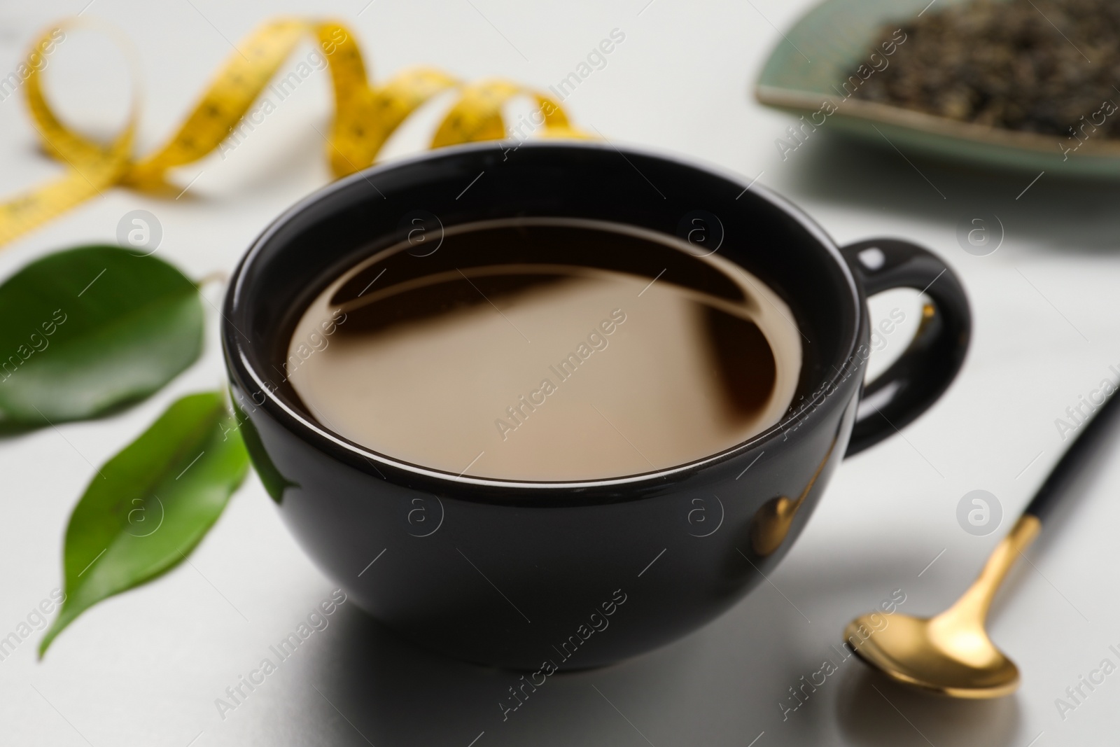 Photo of Cup of herbal diet tea and spoon on light table, closeup. Weight loss concept