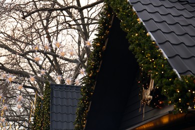 Photo of Christmas fair stall roof decorated with beautiful festive lights and pine garland outdoors