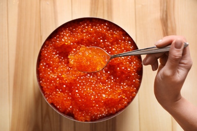 Photo of Woman holding spoon with fresh red caviar at wooden table, top view