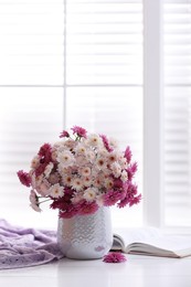 Photo of Beautiful bouquet and open book on white wooden table near window