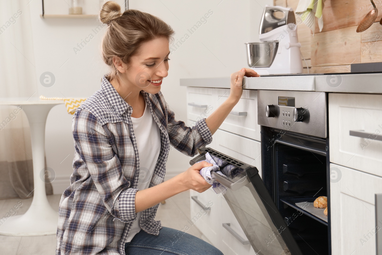 Photo of Young woman baking cookies in oven at home