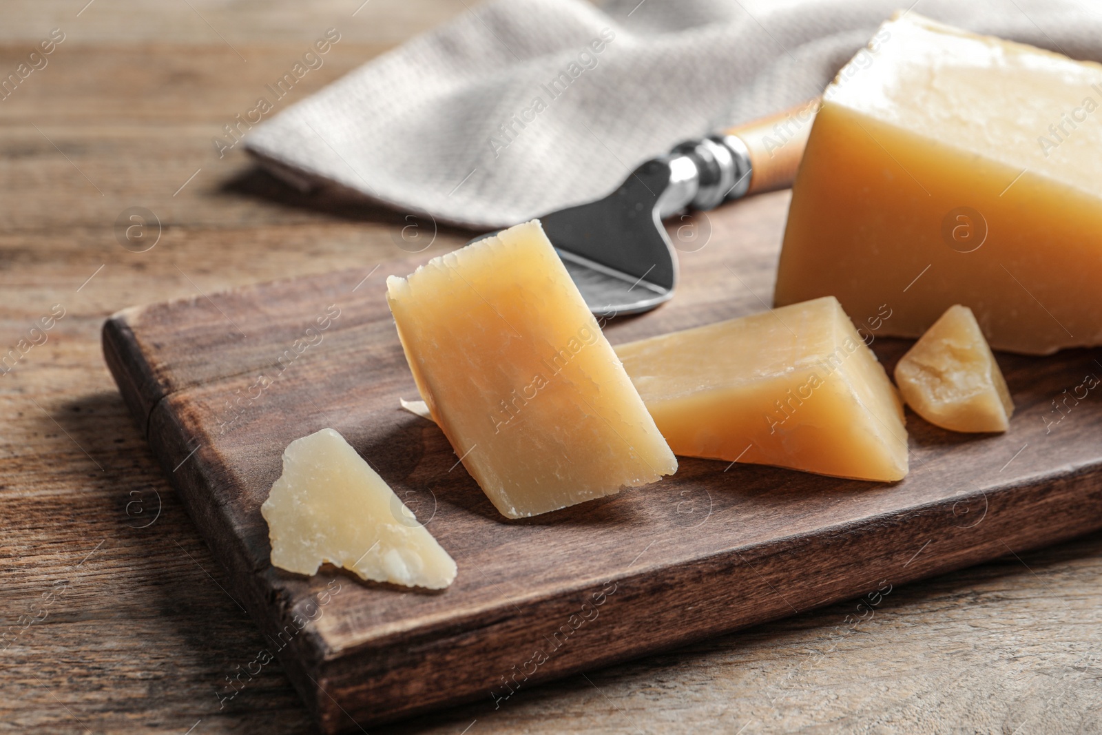 Photo of Board with cut Parmesan cheese on wooden table