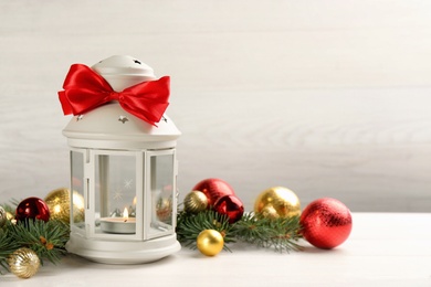 Photo of Christmas lantern with burning candle and festive decor on white wooden table. Space for text