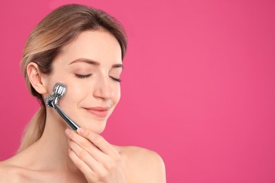 Young woman using metal face roller on pink background, space for text