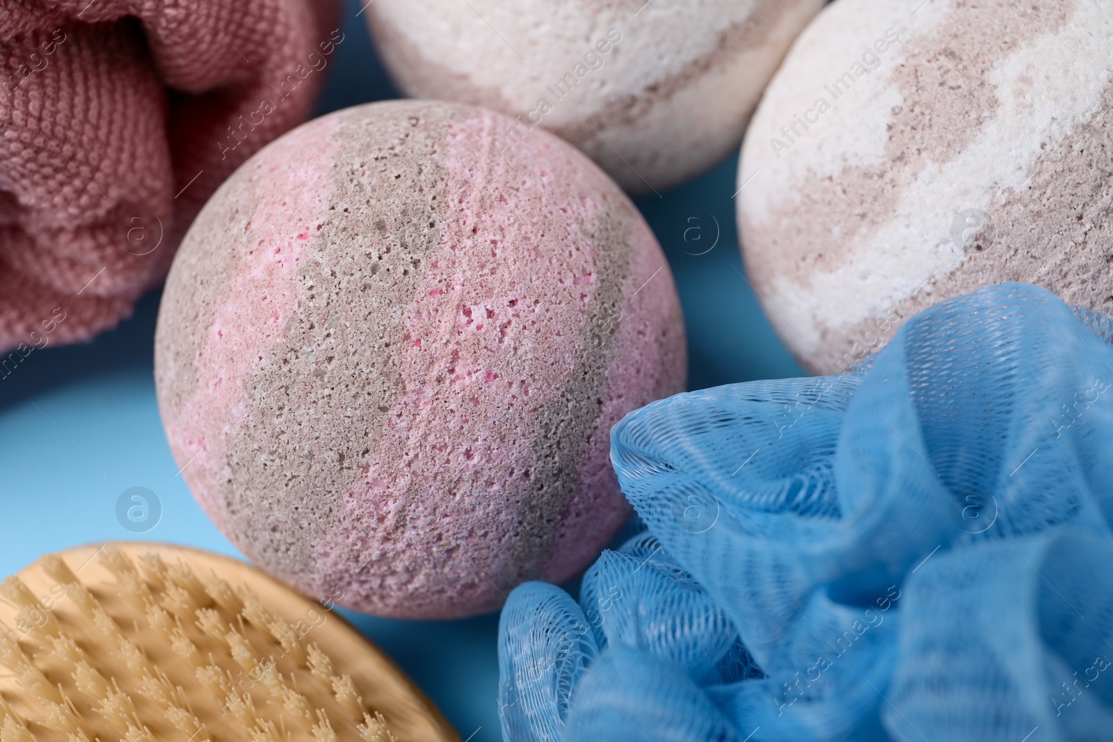 Photo of Bath bombs, massage brush and towel on light blue background, closeup