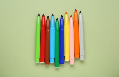 Photo of Different colorful markers on light green background, flat lay