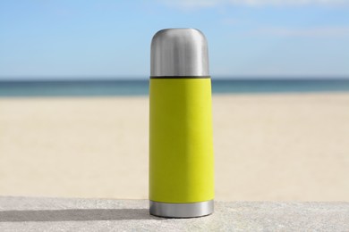 Photo of Metallic thermos with hot drink on stone surface near sea