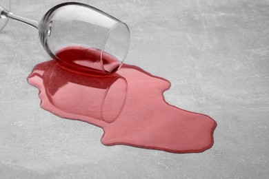 Glass with spilled red wine on light grey surface, closeup