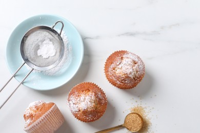 Photo of Delicious sweet muffins, plate and sieve on white marble table, flat lay, Space for text