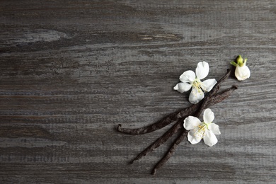 Flat lay composition with aromatic vanilla sticks and flowers on wooden background, space for text