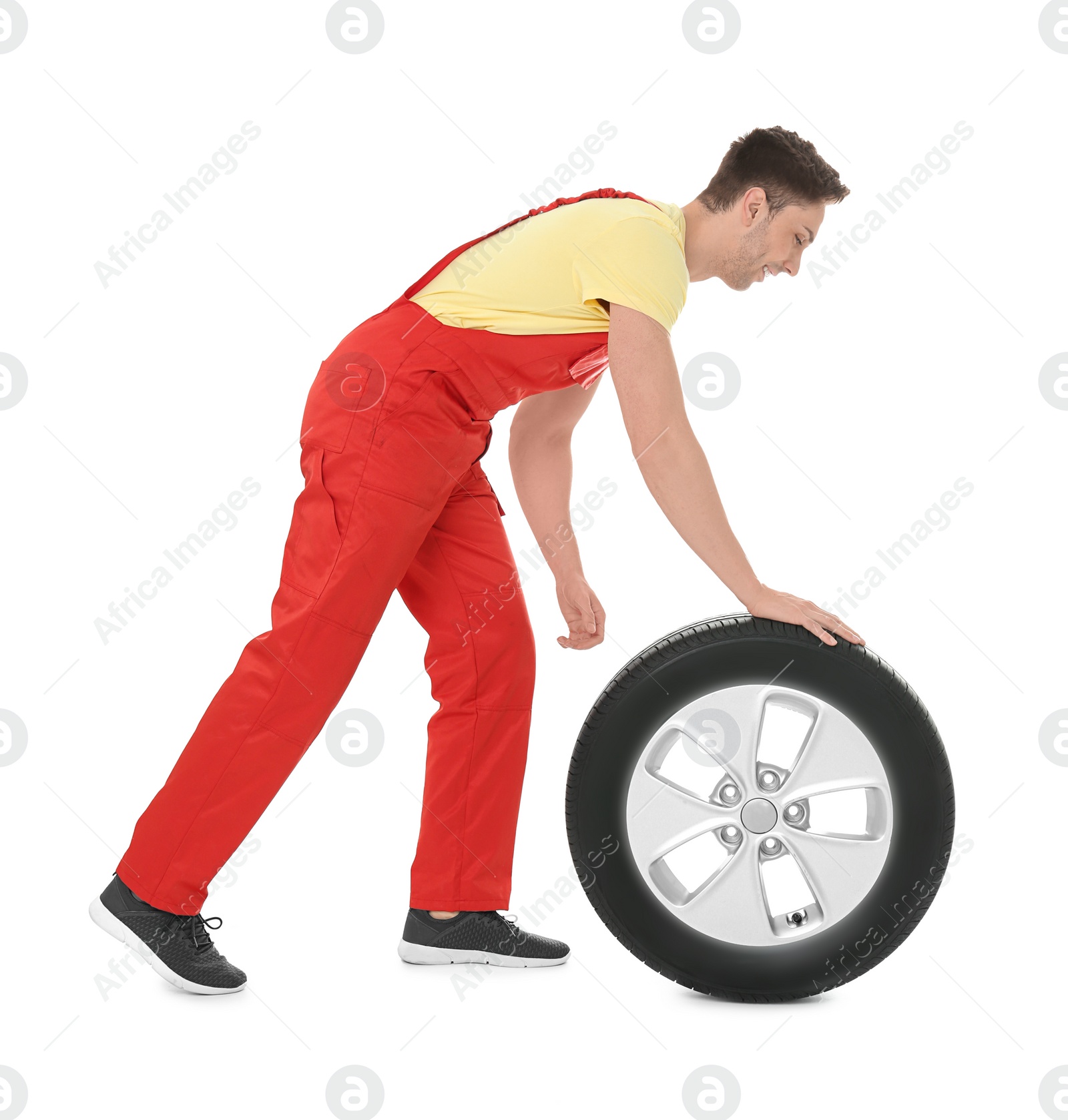 Photo of Young mechanic in uniform with car tire on white background