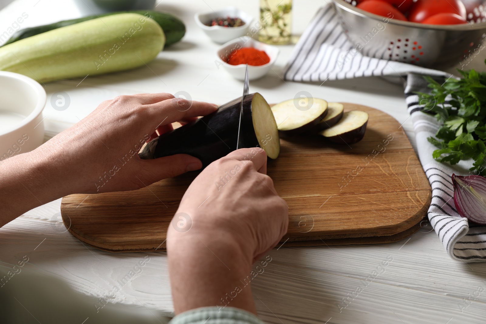 Photo of Cooking delicious ratatouille. Woman cutting fresh eggplant at white wooden table, closeup