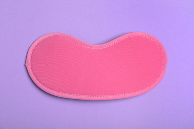 Photo of Pink sleeping mask on violet background, top view. Bedtime accessory