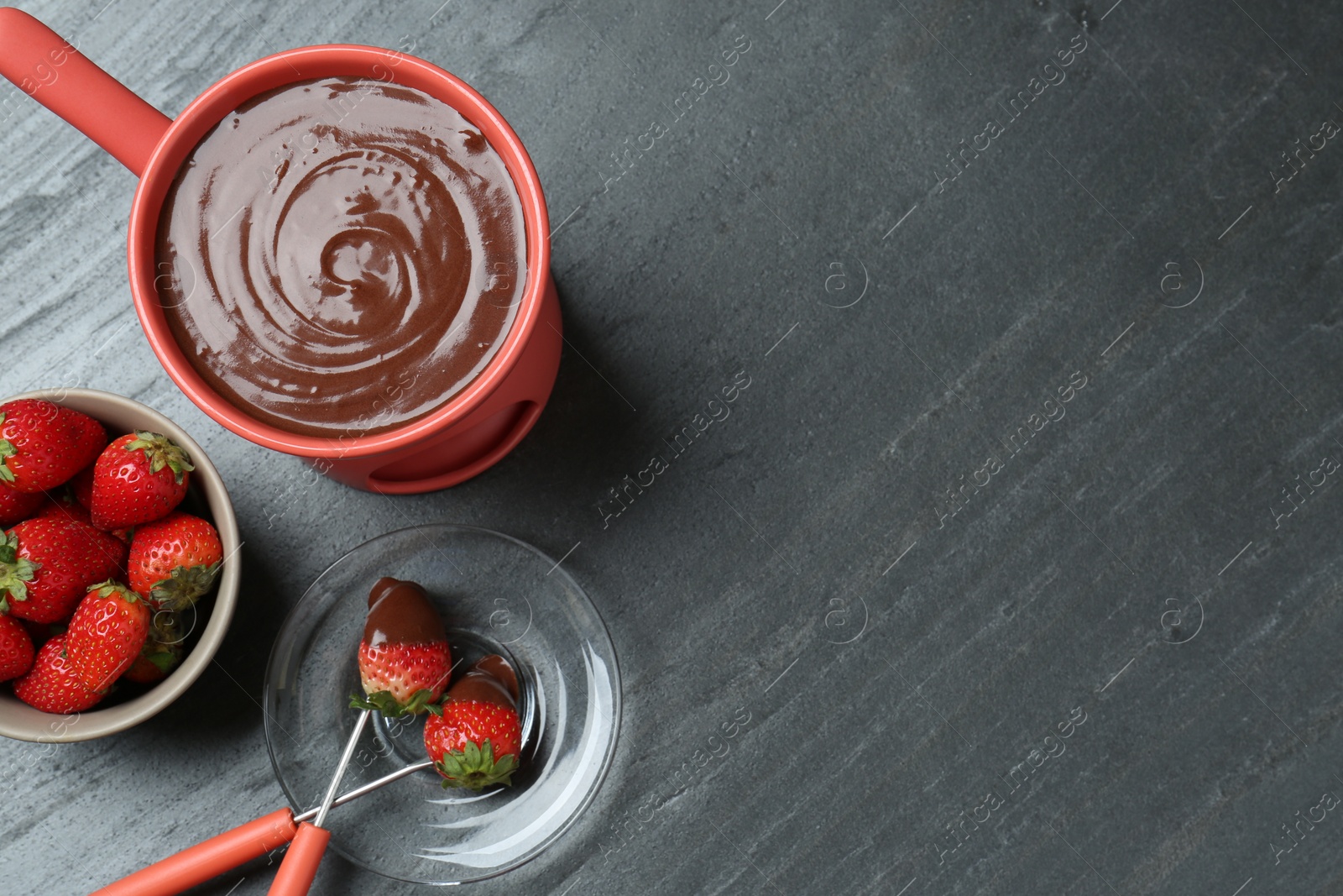 Photo of Fondue pot with melted chocolate, fresh strawberries and forks on grey table, flat lay. Space for text