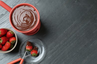 Photo of Fondue pot with melted chocolate, fresh strawberries and forks on grey table, flat lay. Space for text