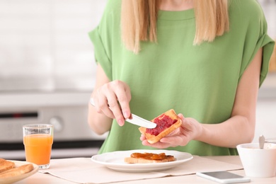 Photo of Beautiful woman eating tasty toasted bread with jam at table