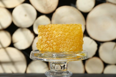 Photo of Glass stand with natural honeycomb near woods, closeup