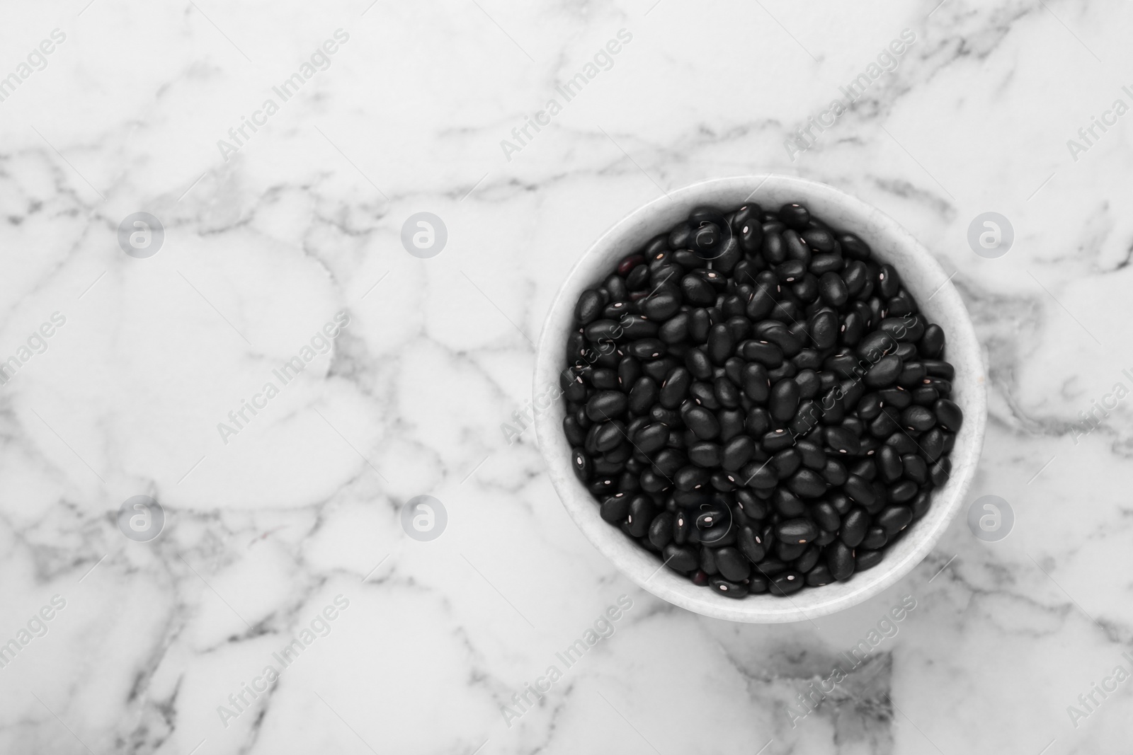 Photo of Bowl of raw black beans on white marble table, top view. Space for text