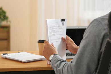 Man working with documents at wooden table in office, closeup