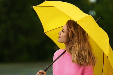 Happy young woman with bright umbrella under rain outdoors