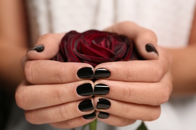 Photo of Woman with black manicure holding rose, closeup. Nail polish trends