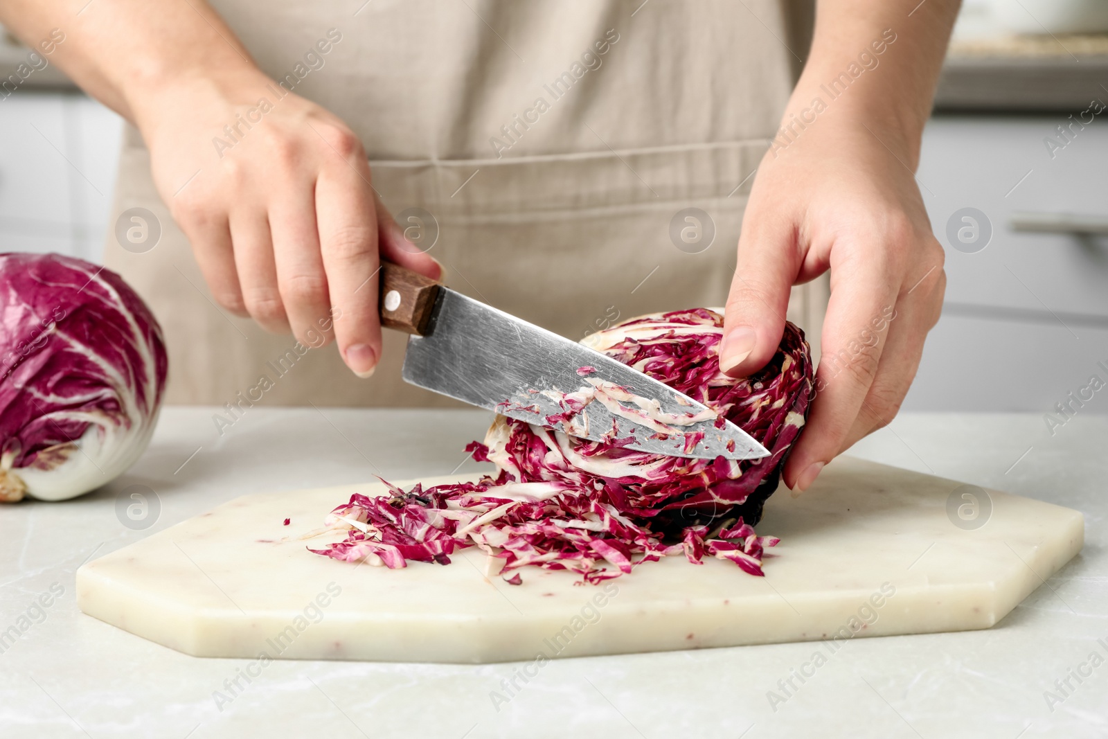 Photo of Woman cutting fresh ripe radicchio at light table, closeup