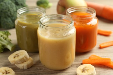 Tasty baby food in jars and ingredients on light wooden table, closeup