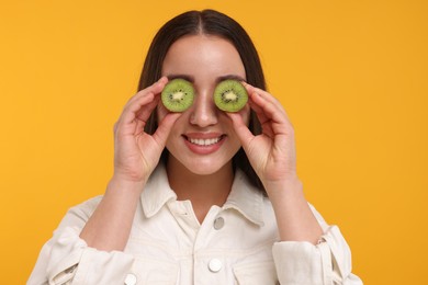 Photo of Woman covering eyes with halves of kiwi on yellow background
