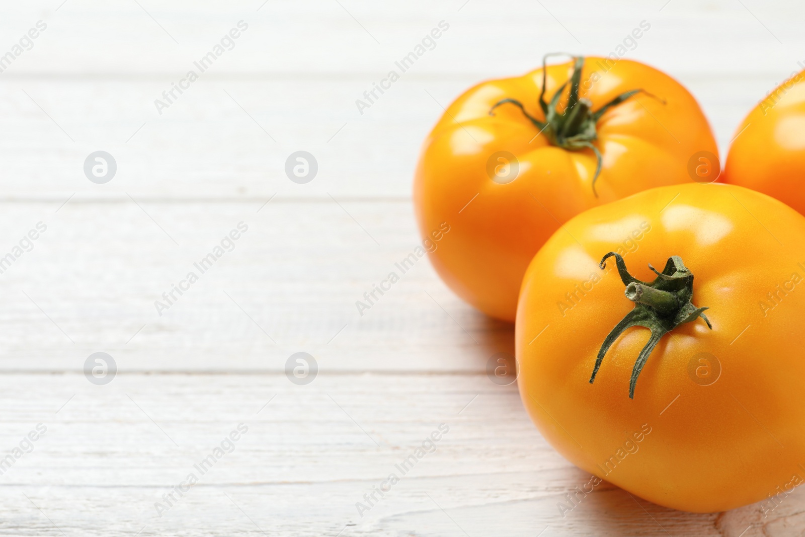 Photo of Fresh ripe yellow tomatoes on white wooden table, closeup. Space for text