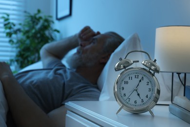 Photo of Sleepy man in bed at home, focus on alarm clock. Space for text
