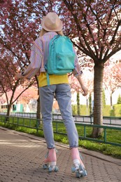 Photo of Young woman roller skating in spring park, back view