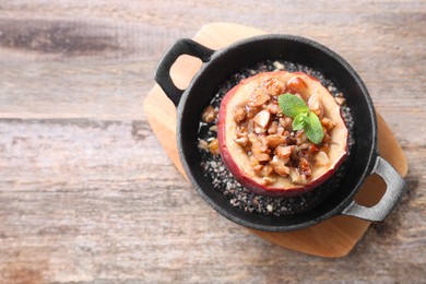 Photo of Tasty baked apple with nuts, honey and mint in baking dish on wooden table, top view. Space for text