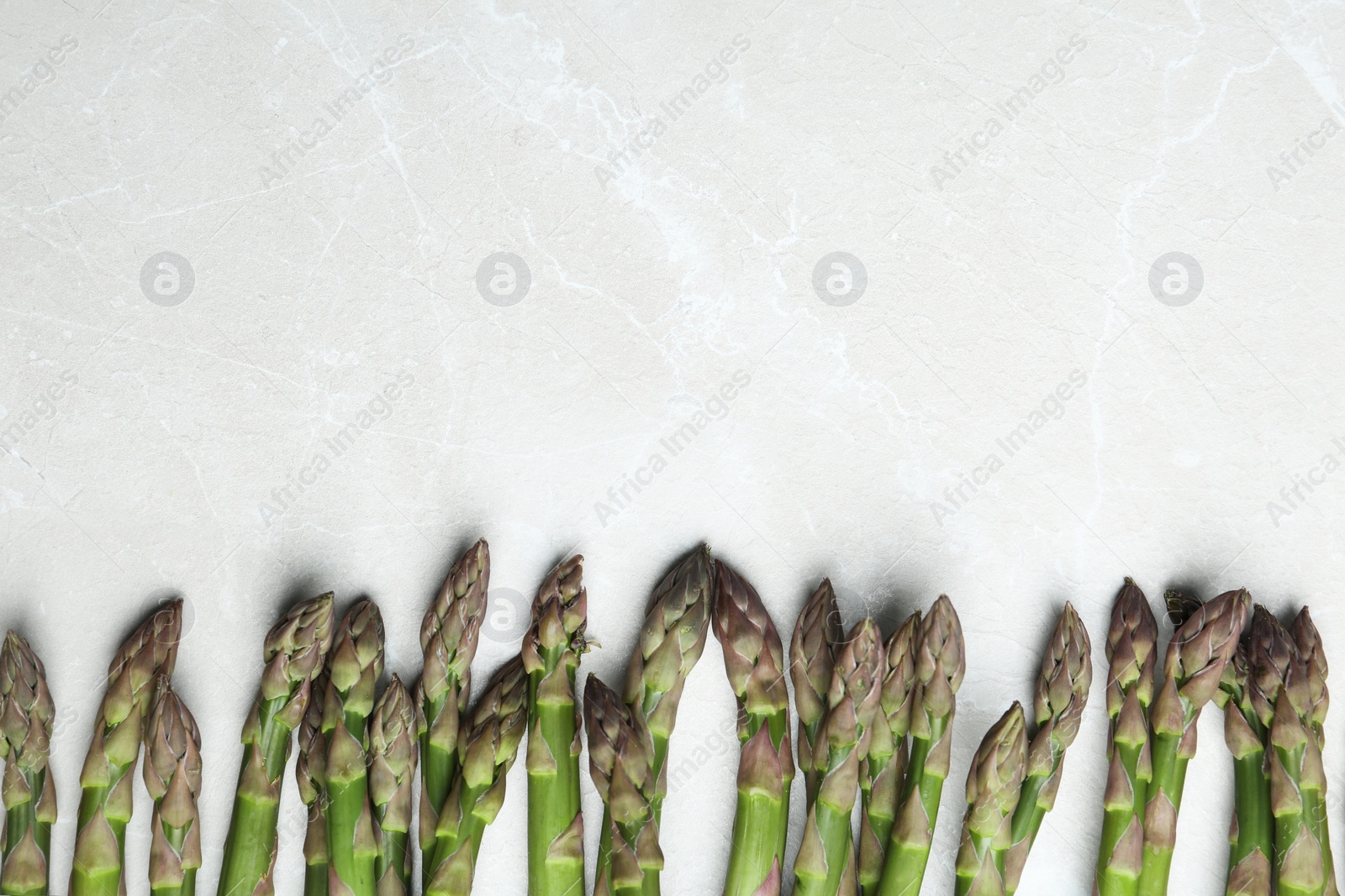 Photo of Fresh raw asparagus on light grey marble table, flat lay. Space for text