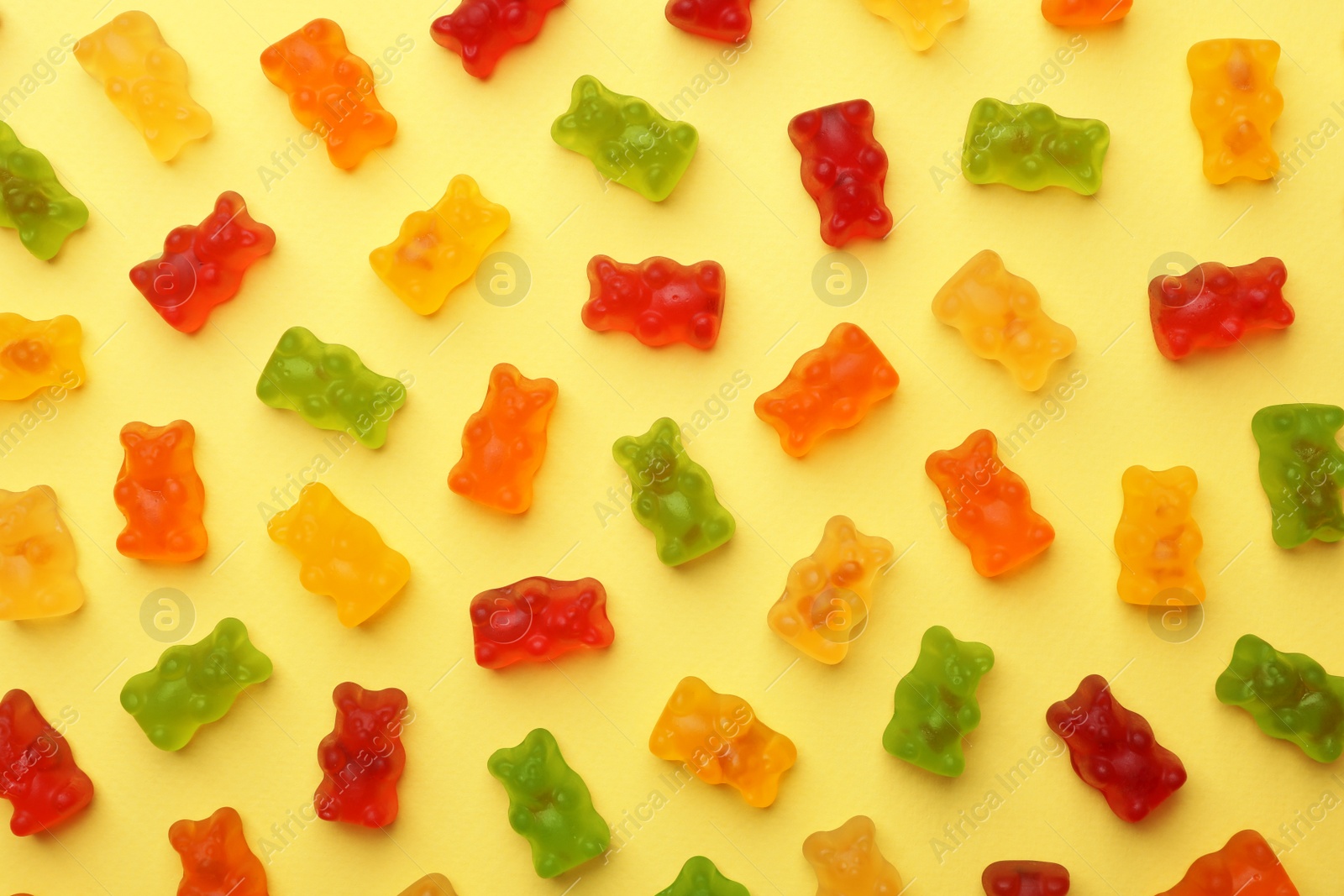 Photo of Delicious bright jelly bears on yellow background, flat lay