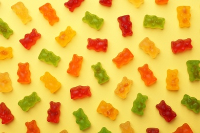 Photo of Delicious bright jelly bears on yellow background, flat lay