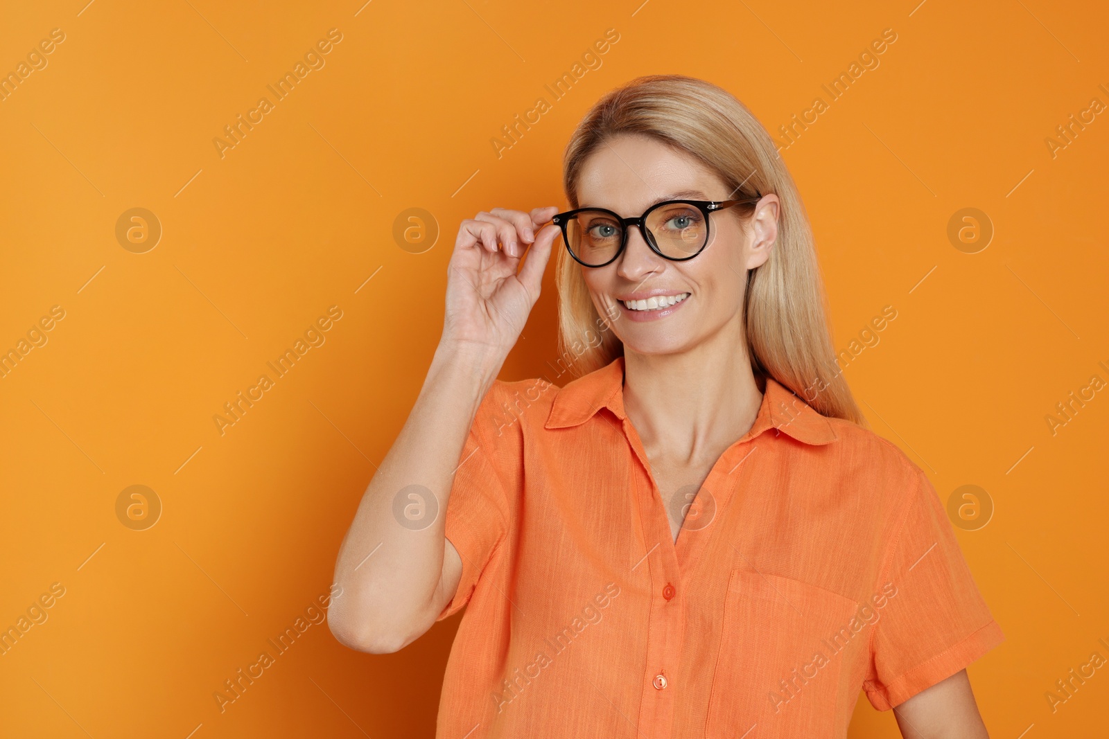 Photo of Portrait of smiling woman in stylish glasses on orange background. Space for text