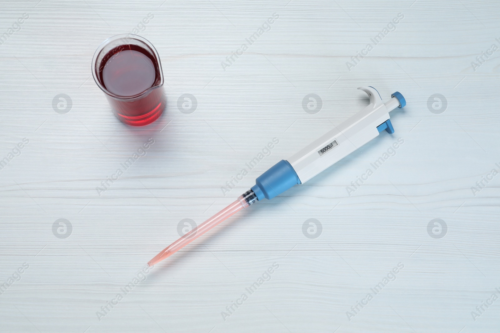 Photo of Laboratory analysis. Micropipette and beaker with liquid on white wooden table, top view