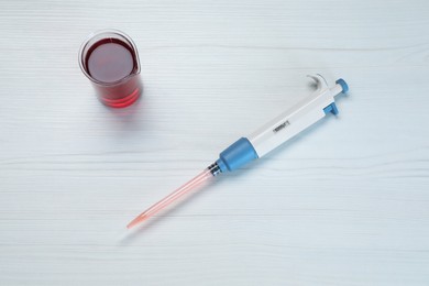 Laboratory analysis. Micropipette and beaker with liquid on white wooden table, top view