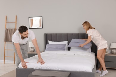 Photo of Couple changing bed linens in room. Domestic chores