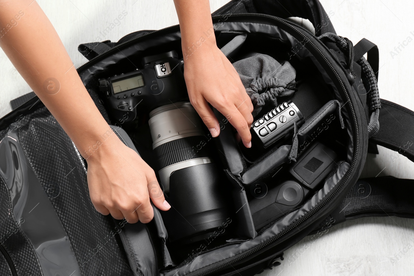 Photo of Woman putting professional photographer's equipment into backpack on floor, top view