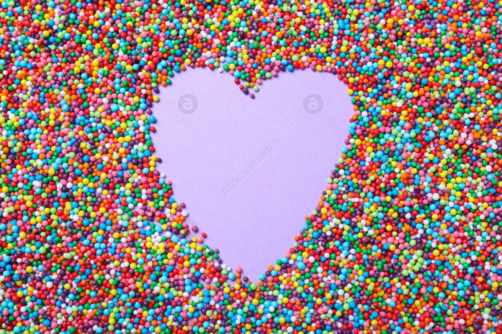 Photo of Heart shaped frame of sprinkles on lilac background, flat lay with space for text. Confectionery decor