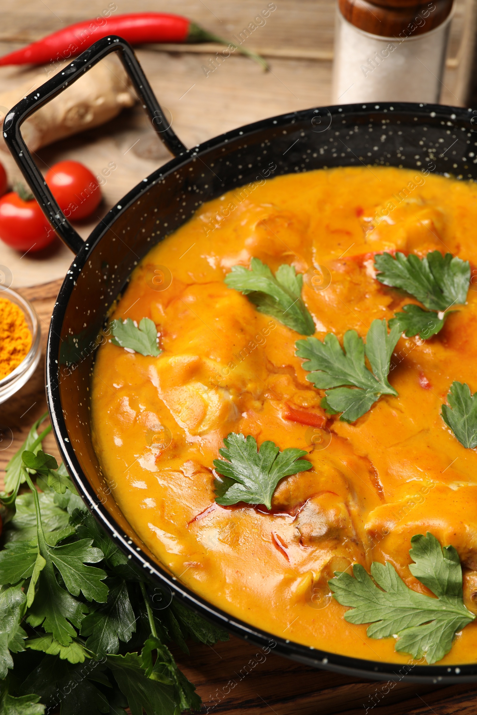 Photo of Tasty chicken curry with parsley and ingredients on wooden table