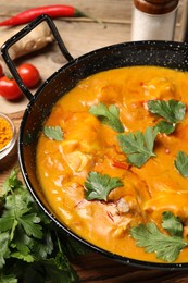 Photo of Tasty chicken curry with parsley and ingredients on wooden table