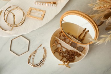 Photo of Jewelry box with mirror and stylish golden bijouterie on white marble table, flat lay