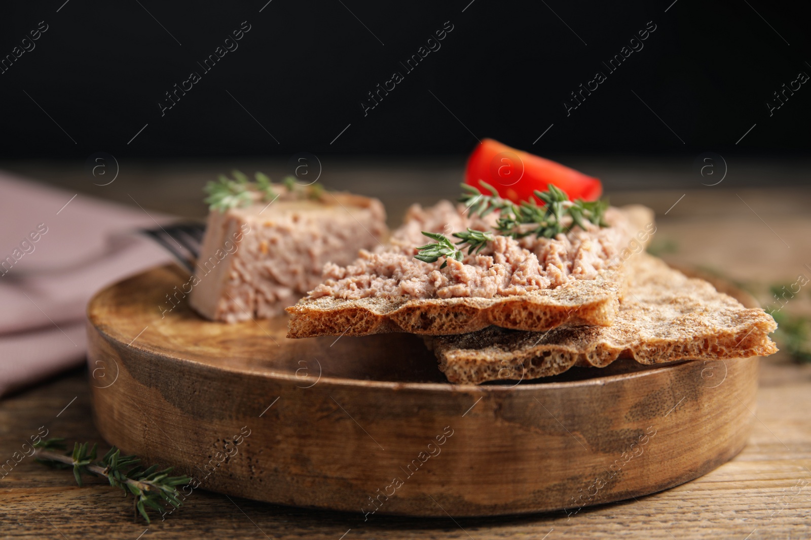 Photo of Crispy crackers with delicious meat pate and thyme served on wooden table, closeup