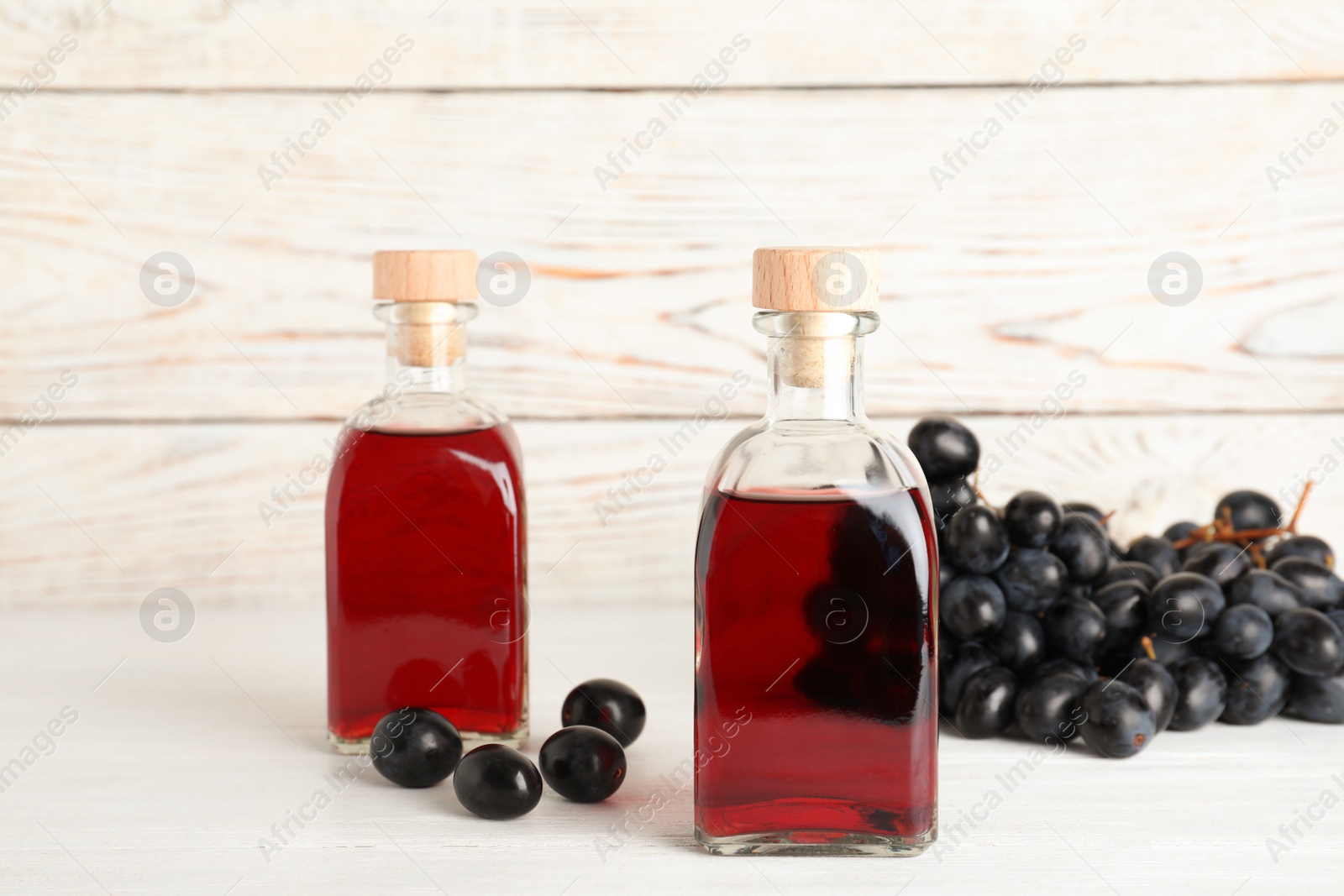 Photo of Glass bottles with wine vinegar and fresh grapes on wooden table