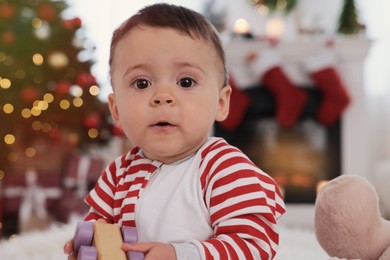 Baby wearing bright pajamas in room decorated for Christmas