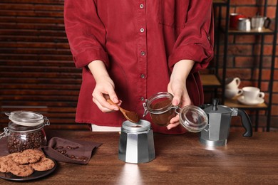 Photo of Woman putting ground coffee into moka pot at wooden table, closeup