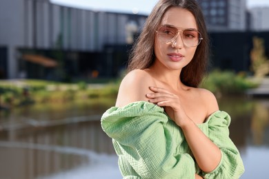 Beautiful woman in sunglasses near river, space for text