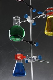 Retort stand and laboratory flasks with liquids on grey background